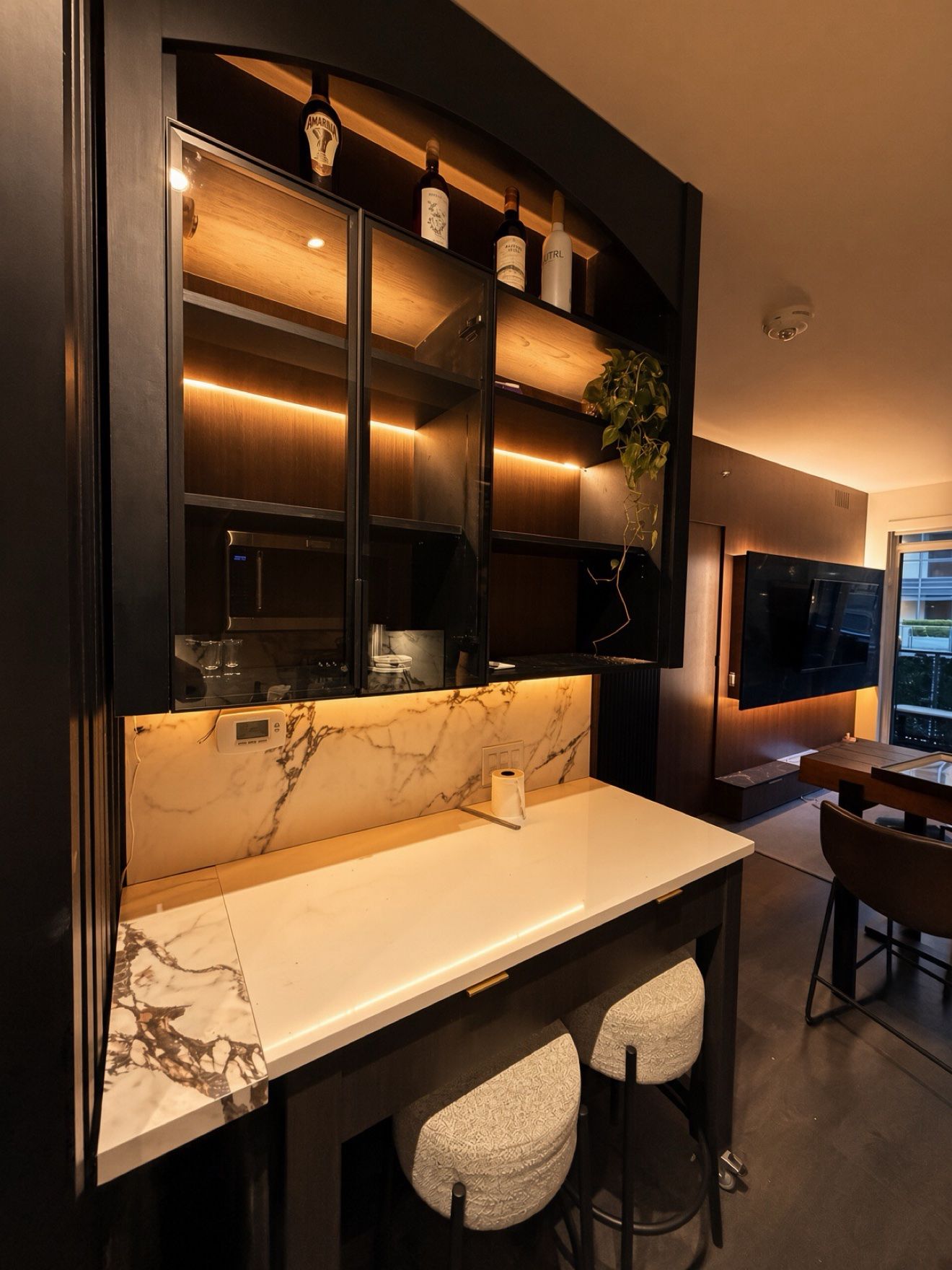 Black custom bar with glass cabinets, LED shelving and marble backsplash