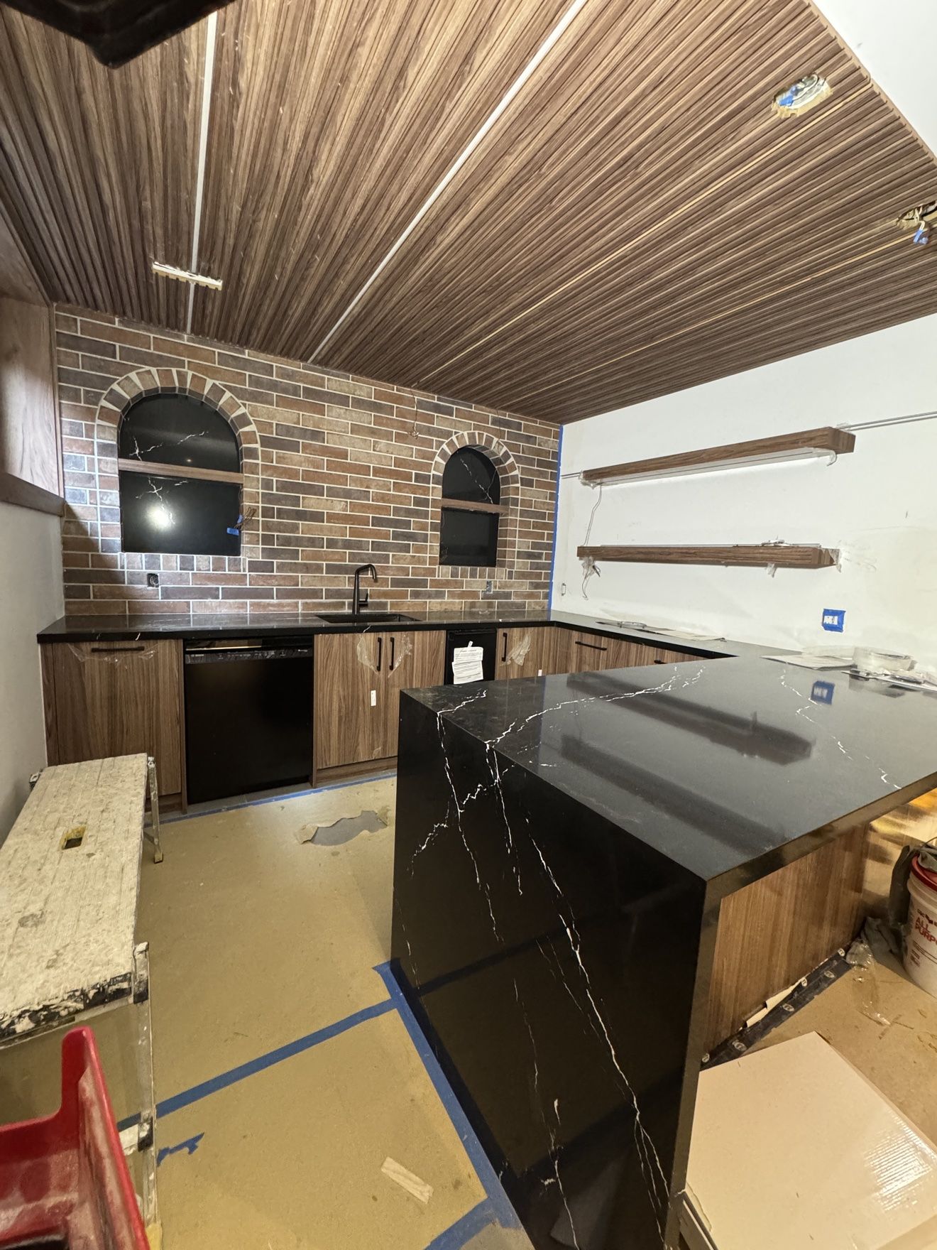 Basement bar with brick wall, arched niches, walnut slat ceiling and black marble island