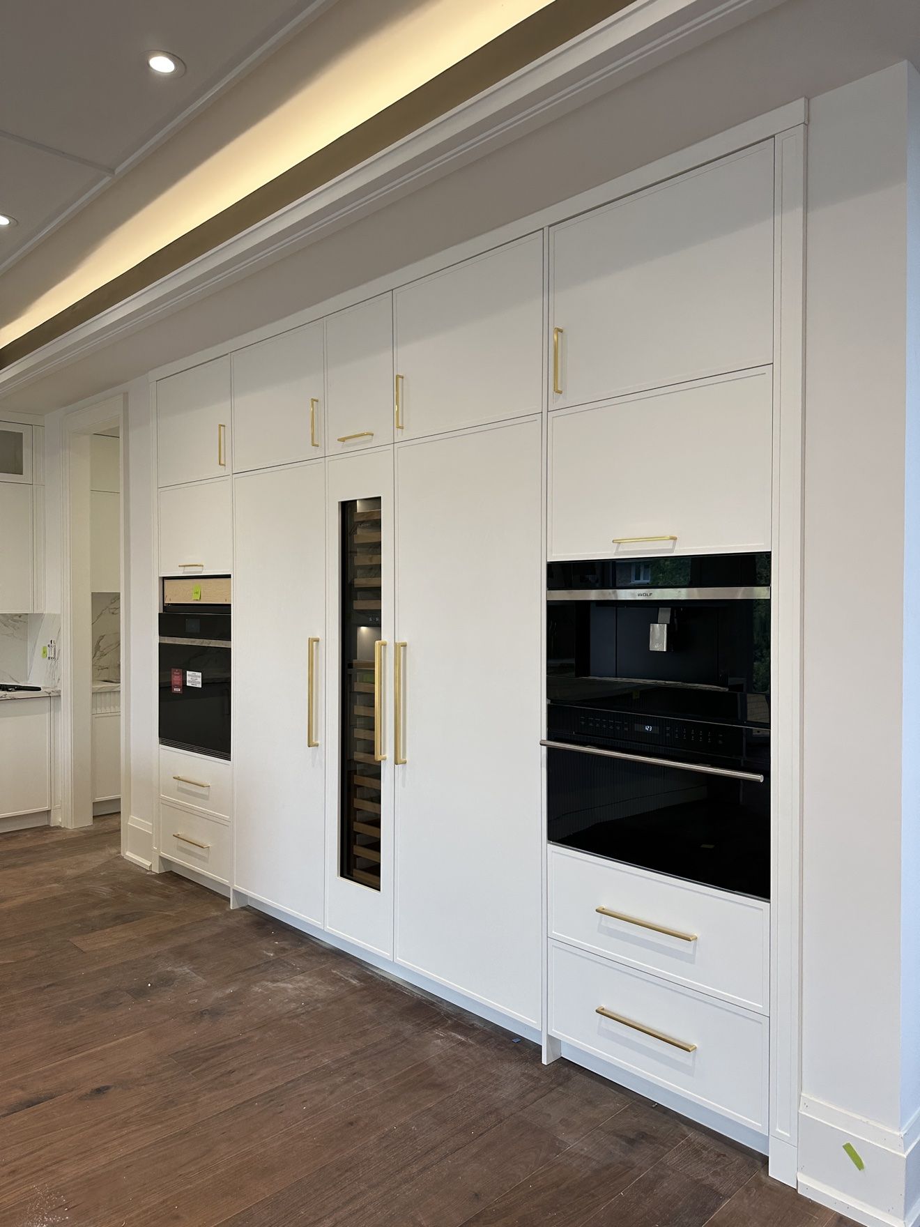 White appliance wall with integrated wine column, wall ovens and brass hardware