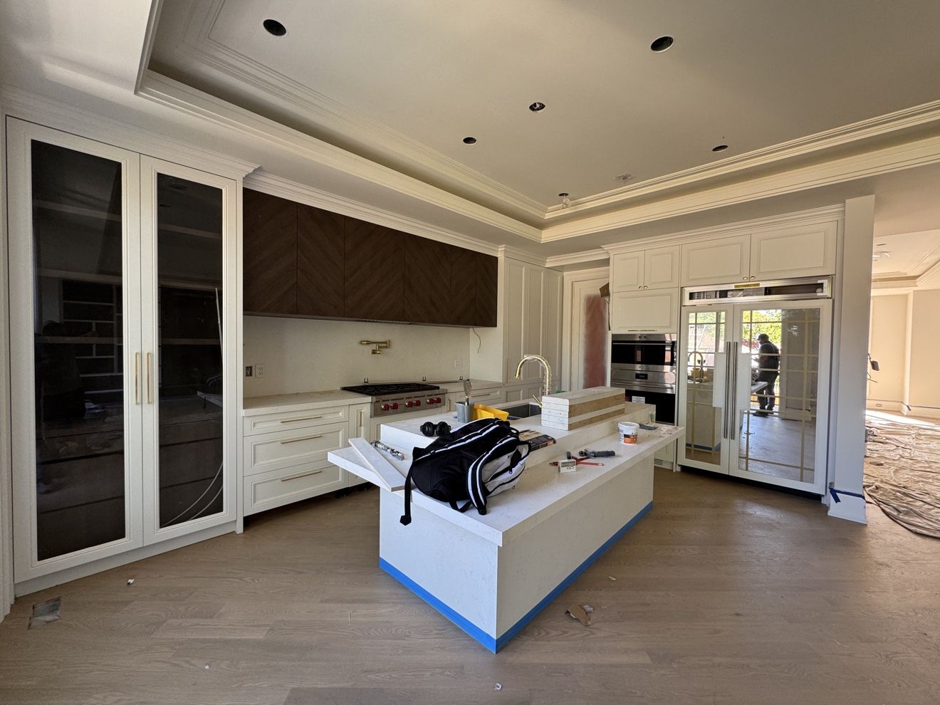 Kitchen during installation with chevron walnut uppers and glass pantry doors