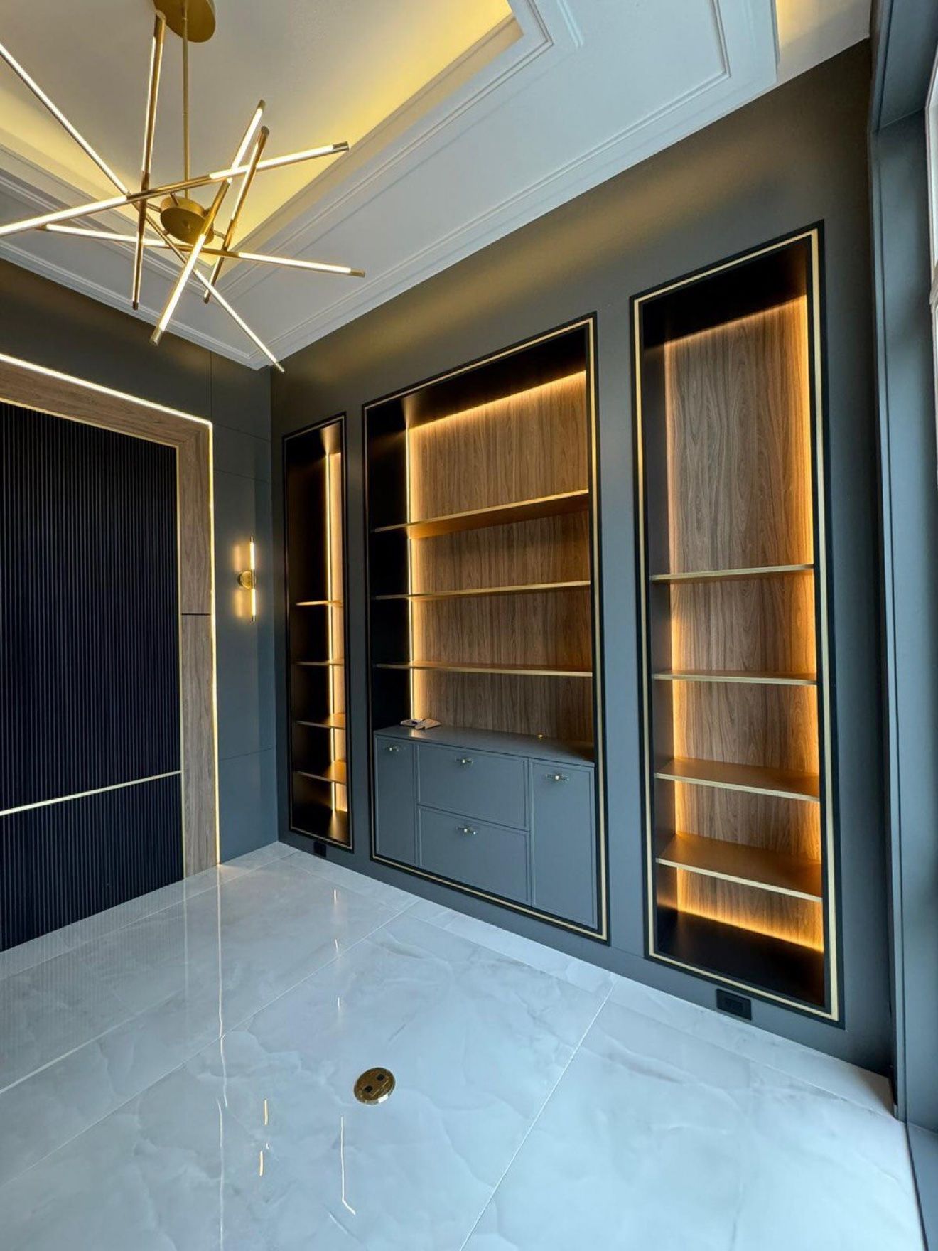 Library wall with backlit walnut display niches and brass trim