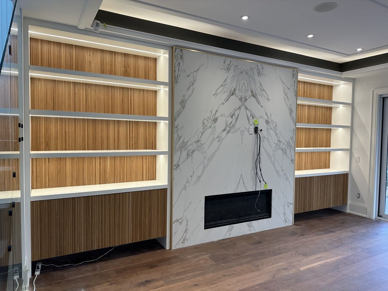Book-matched marble fireplace wall flanked by fluted walnut built-ins with LED shelf lighting