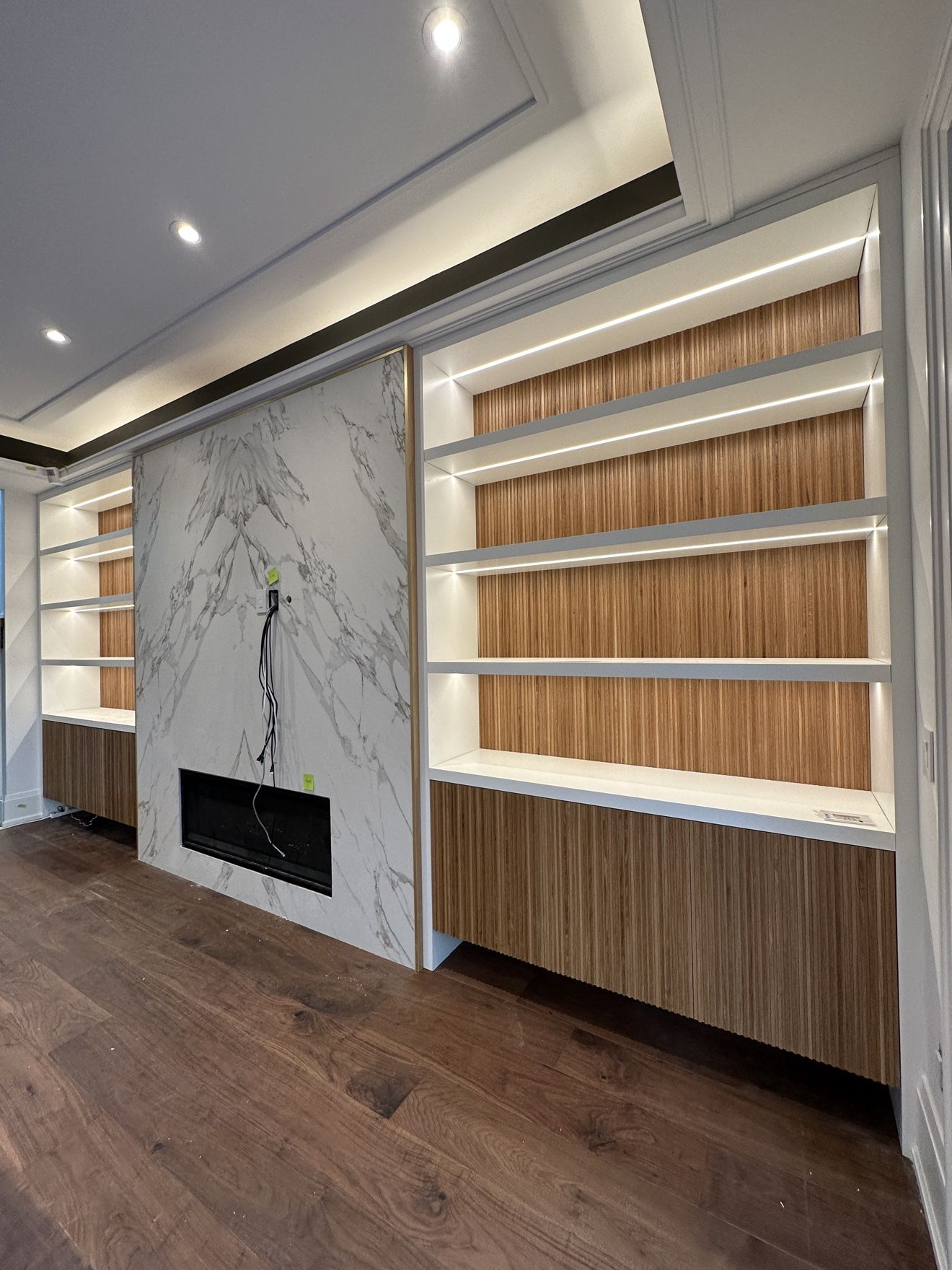 Fluted walnut display shelves with hidden LED lighting beside a marble fireplace wall
