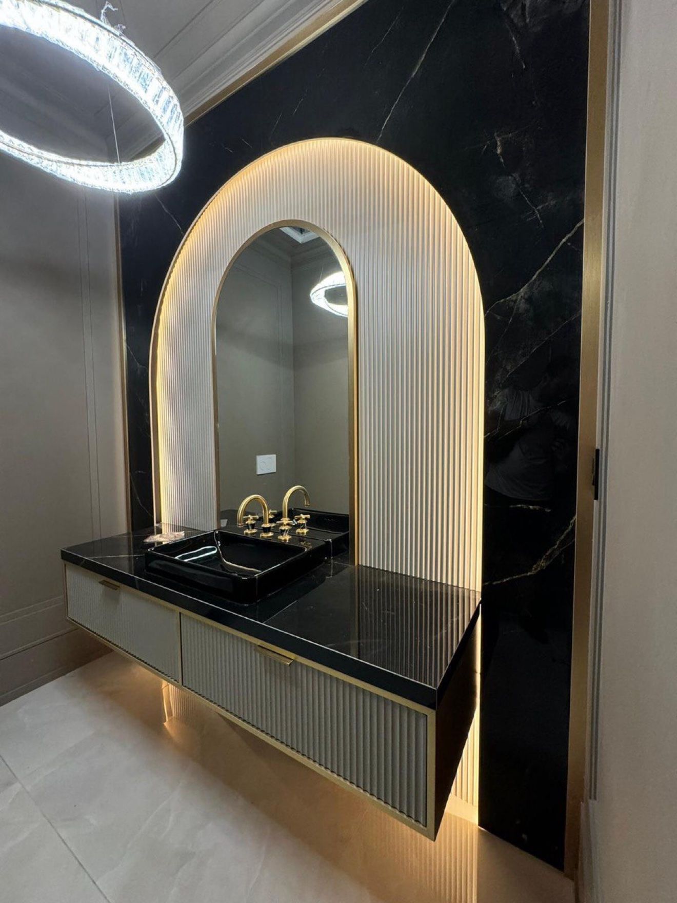 Powder room with backlit arched fluted mirror panel and black marble