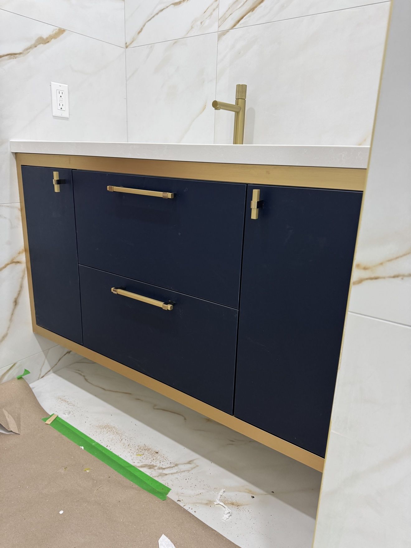 Navy floating vanity with brass frame and hardware in marble tile bath